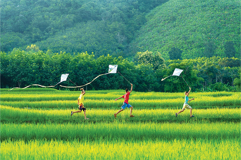 Children run across rice fields with their Pakpao kites