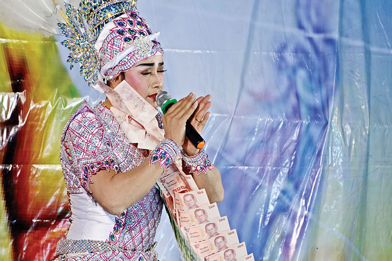 A performer wears garlands of banknotes — gifts from Mae Yok and the audience